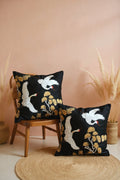 Decorative pillows with bird and floral patterns on a chair against a beige wall.