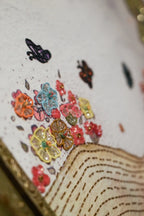 Close-up of a decorative item with colorful flowers and butterflies on a white background.