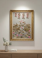 Decorative wall art with floral elements in a gold frame on a light gray wall.