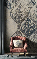 Pink armchair with a decorative pillow against a patterned wall.