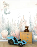 Children's room with mermaid wall mural, toy car, teddy bear, and wooden dresser.